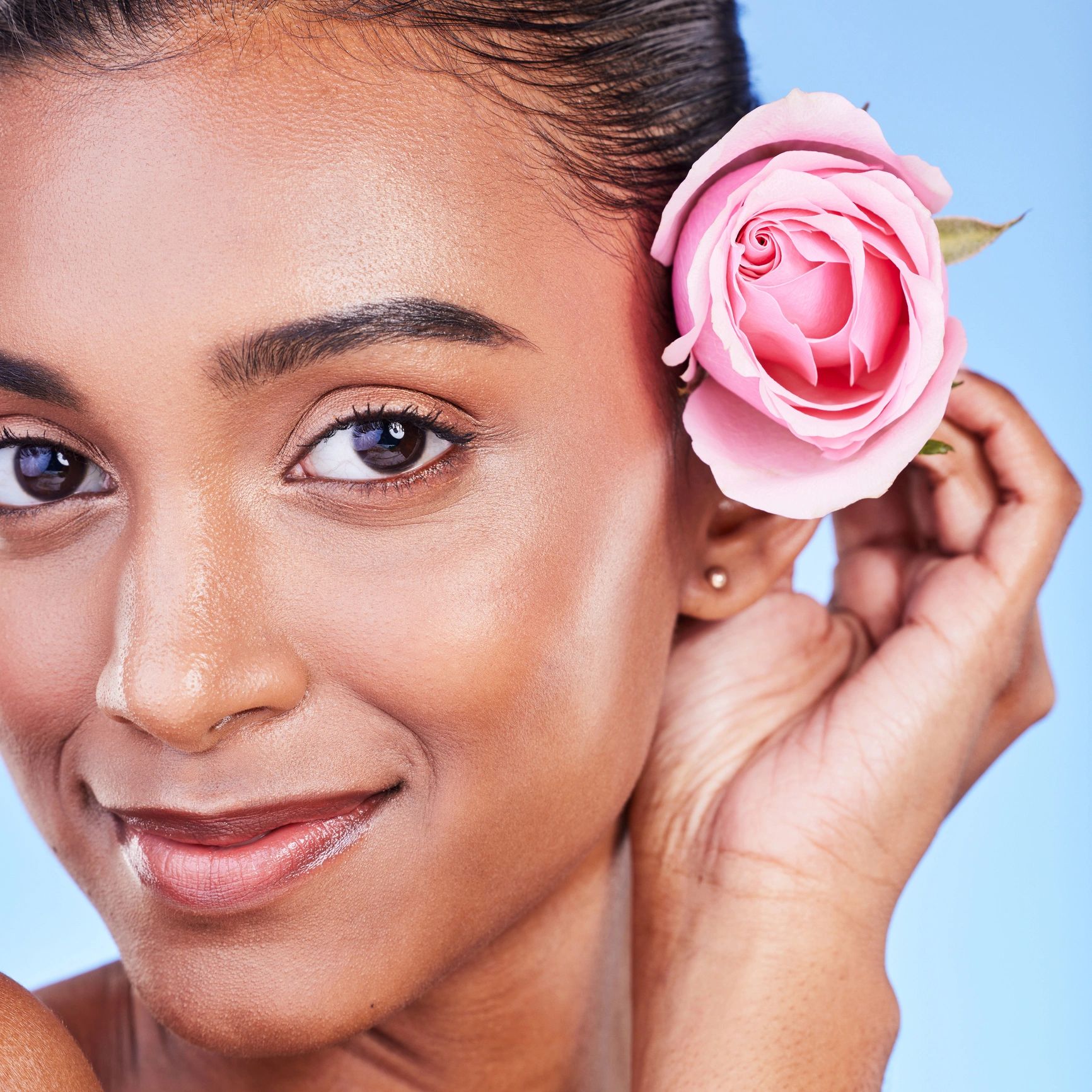 Rose, portrait and skincare of woman in studio for eco cosmetics, natural glow and aesthetic on blue background. Face, happy indian model and flowers for beauty, sustainability or floral dermatology